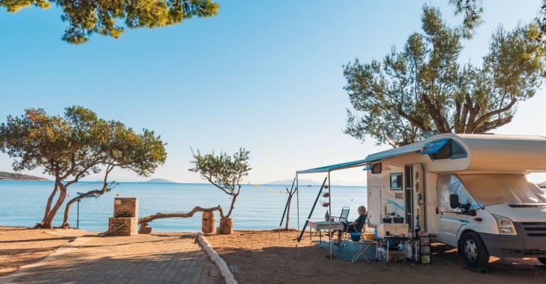 Familie die met een camper reist, eet ontbijt op een strand.